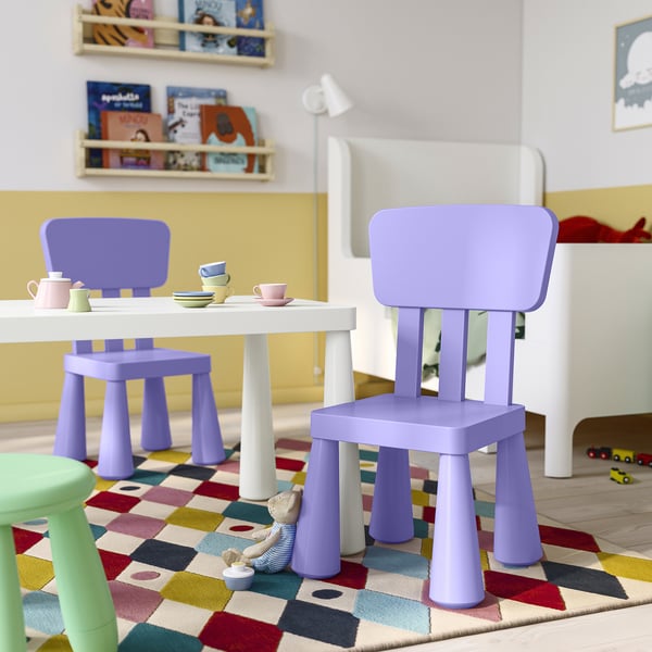 Área de xogo infantil con cadeiras MAMMUT púrpuras, mesa branca, alfombra colorida e configuración de xoguetes; As cadeiras púrpuras son pequenas e lixeiras.