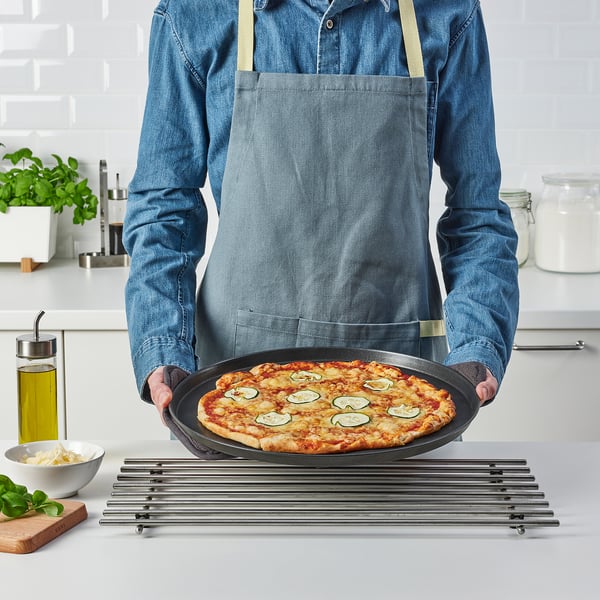 Persoa que sostén unha pizza nunha bandexa redonda nunha cociña. A bandexa ten mangos para un fácil manexo.