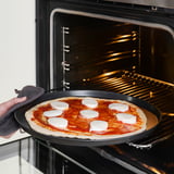 Poñer a pizza non cocida no forno. 6 anacos de queixo sobre salsa vermella e masa. Luz do forno acendida, estante baleira.