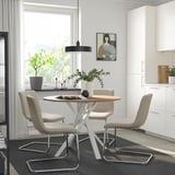 Zona de comedor moderna con mesa redonda, cadeiras grises e grandes fiestras.