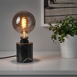 Unha lámpada de mesa cunha base de mármore negro e unha lámpada brillante, proporcionando iluminación de humor.