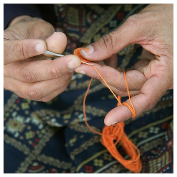 Persoa que crochet fíos laranxas. Mans centradas na elaboración de deseño intrincado.