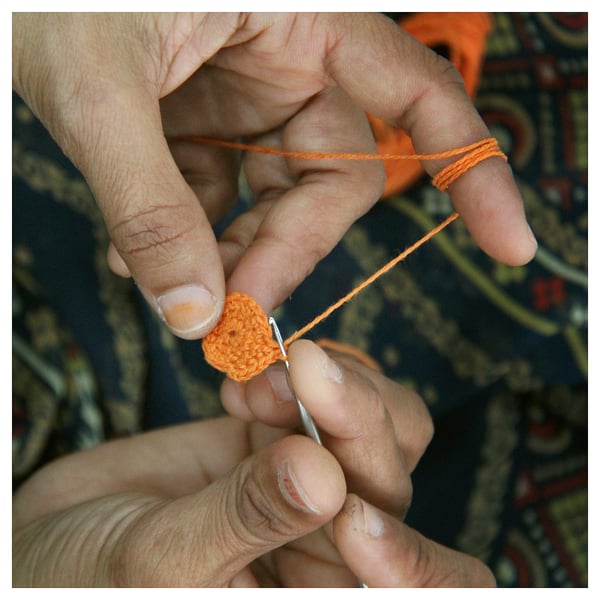 Mans elaboradas con fío laranxa. Fío a través da agulla, pequena peza de crochet formada.