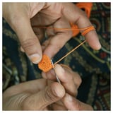 Mans elaboradas con fío laranxa. Fío a través da agulla, pequena peza de crochet formada.