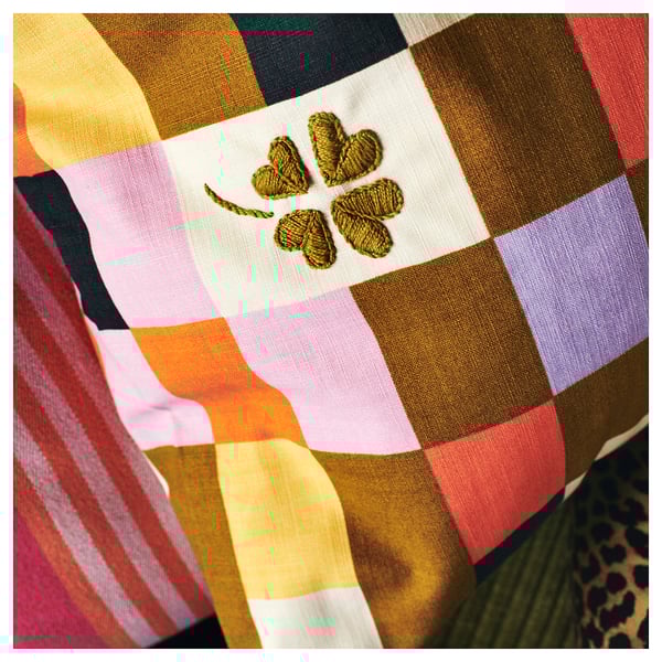Coxín de cadros multicolor MÄVINN con trevo de catro follas bordado dourado.