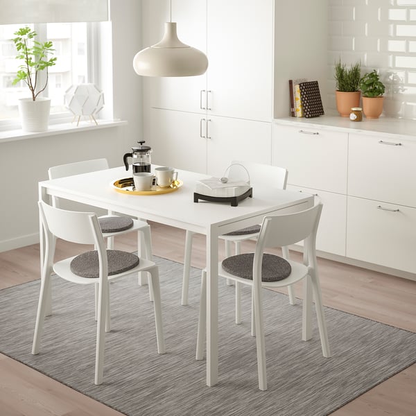 Mesa de comedor branca MELLTORP con 4 cadeiras de almofada negra, configuración de café, alfombra gris, nunha cociña luminosa con plantas.