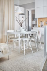 Conxunto de comedor MELLTORP con mesa resistente á humidade e cadeiras apilables. A luz colgante e o vaso con ramas crean un espazo acolledor e minimalista.