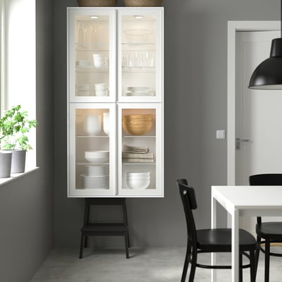 Cociña moderna con armario branco, portas de vidro, taburete negro, cadeiras, plantas.