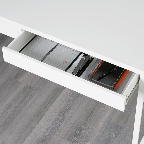 Caixón de escritorio branco aberto revelando cadernos e planificador. A superficie reflectante no interior da parte traseira mostra equipos de oficina.