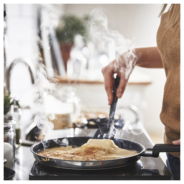 Unha persoa está a cociñar panqueiques nunha tixola MIDDAGSMAT. O vapor está subindo. A tixola está nunha estufa.