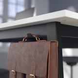 A bolsa de coiro marrón colga nunha mesa negra con estante e ganchos, mostrando almacenamento e organización.