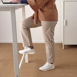 Persoa de pé na mesa alta con repousapés incorporado, usando portátil. Ideal para traballos rápidos e en movemento ou reunións.