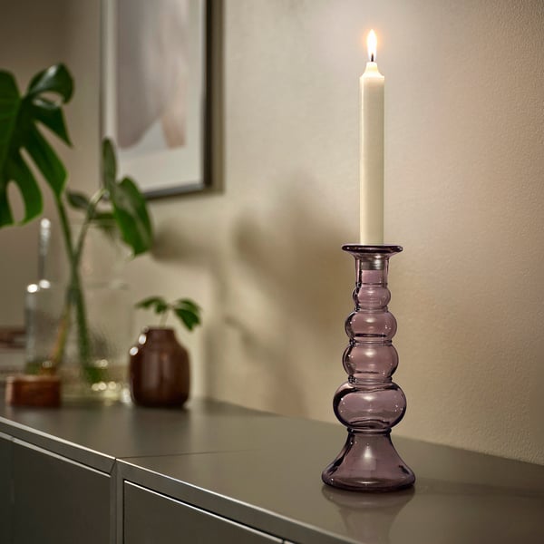 Candelabro de vidro reciclado púrpura con vela no taboleiro, rodeado de decoración.