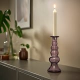 Candelabro de vidro reciclado púrpura con vela no taboleiro, rodeado de decoración.