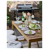 Conxunto de comedor ao aire libre con mesa de madeira, cadeiras de almofada grises, pratos, vasos e flores.