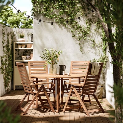 Conxunto de patio exterior con mesa redonda e catro cadeiras de madeira, de cor marrón.