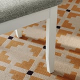 Cadeira moderna con asento tapizado gris e pernas brancas en alfombra con patróns.