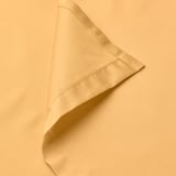 Primeiro plano de saba de cama suave, amarelo dourado que amosa tecido fino e costura limpa.