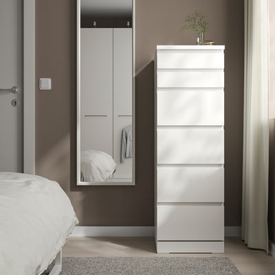 Cofre branco NISSEDAL no dormitorio, seis caixóns, xunto ao armario alto con espello, deseño elegante, decoración minimalista.