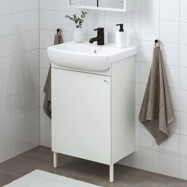 Configuración de baño branco moderno: pequena lavabo vanidade, billa negra, toallas grises. Aforra espazo cun deseño elegante.