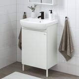 Configuración de baño branco moderno: pequena lavabo vanidade, billa negra, toallas grises. Aforra espazo cun deseño elegante.