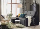 Sala de estar moderna con sofá seccional gris ODENSLUNDA, almofadas de cores, cadeira de vimbio e gran xanela con cortinas con patróns.