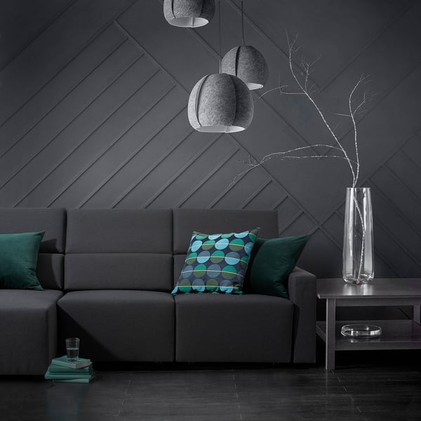 Sala de estar moderna, un sofá gris ODENSLUNDA con almofadas azuladas, lámpadas colgantes grises e un vaso transparente con ramas.