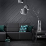 Sala de estar moderna, un sofá gris ODENSLUNDA con almofadas azuladas, lámpadas colgantes grises e un vaso transparente con ramas.