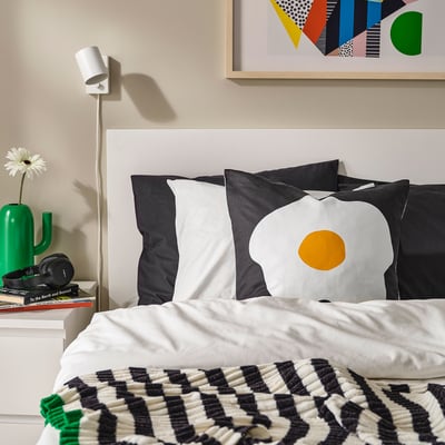 Dormitorio moderno con cama branca, almofadas negras, vaso verde, libros e arte.