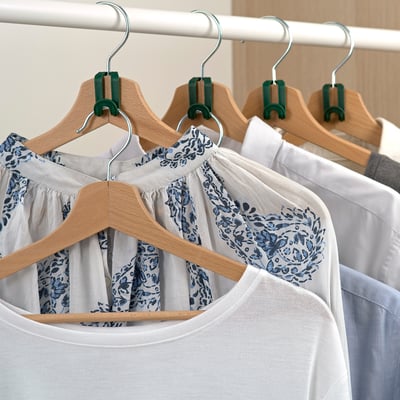 Varias camisetas colgan ordenadamente de colgantes de madeira con ganchos metálicos e clips verdes, permitindo o almacenamento organizado nun armario.