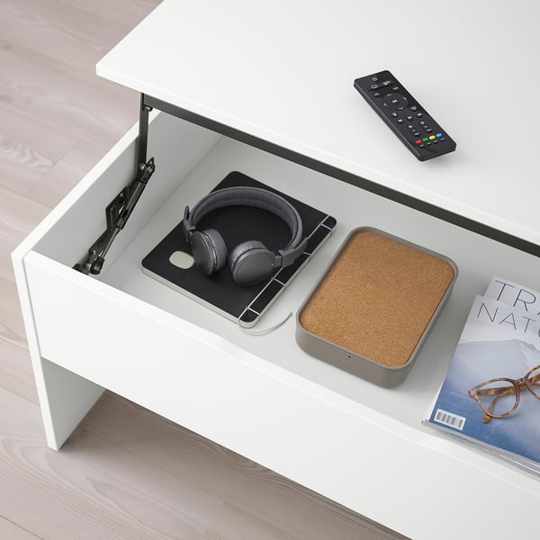 Unha moderna mesa de café axustable cunha parte superior elevable, revelando almacenamento que contén auriculares e un mando a distancia.