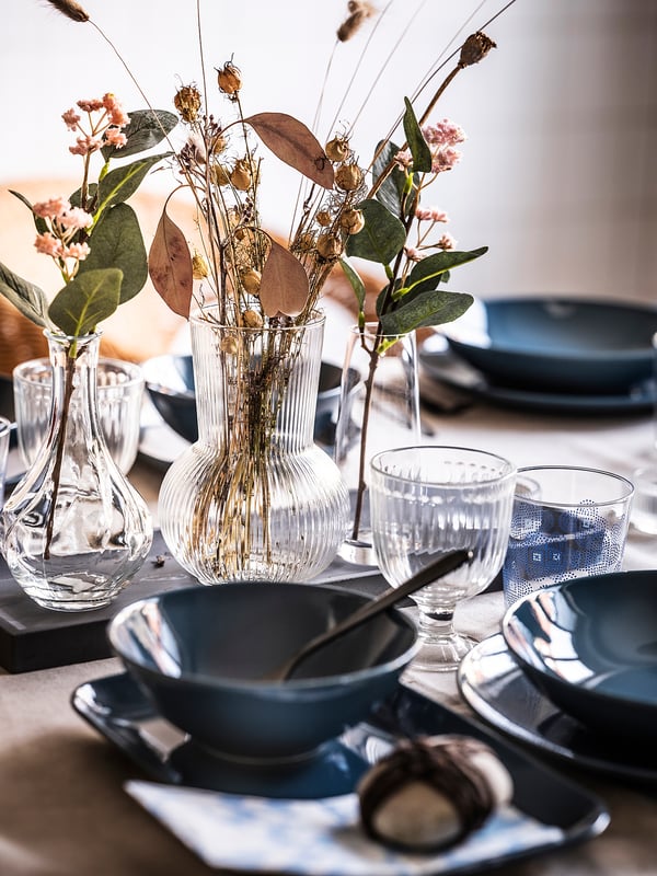 Elegante mesa con vasos de vidro e flores secas; pratos e vasos azuis escuros.