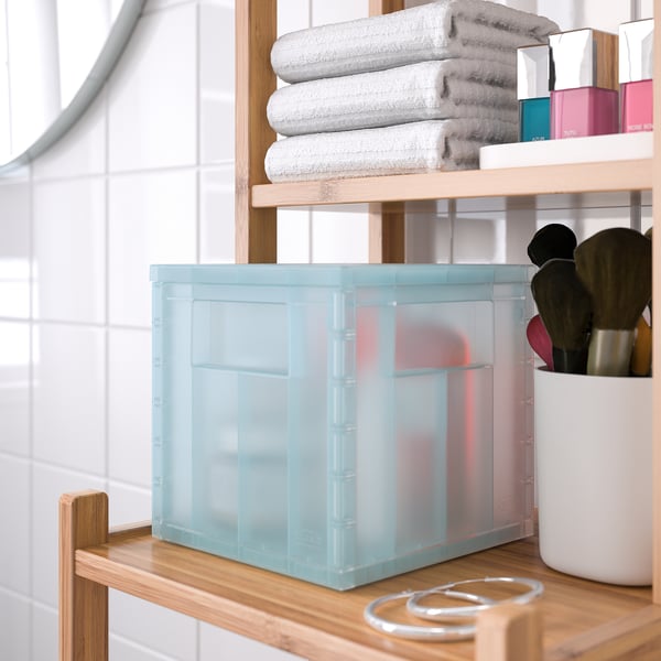 Un estante de baño cunha caixa de almacenamento azul claro, toallas, maquillaxe e cepillos. A caixa mantén os elementos organizados e visibles.