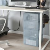 Limpar os caixóns etiquetados baixo monitor, almacenando pequenos obxectos de forma eficiente. Cadeira de oficina gris próxima.