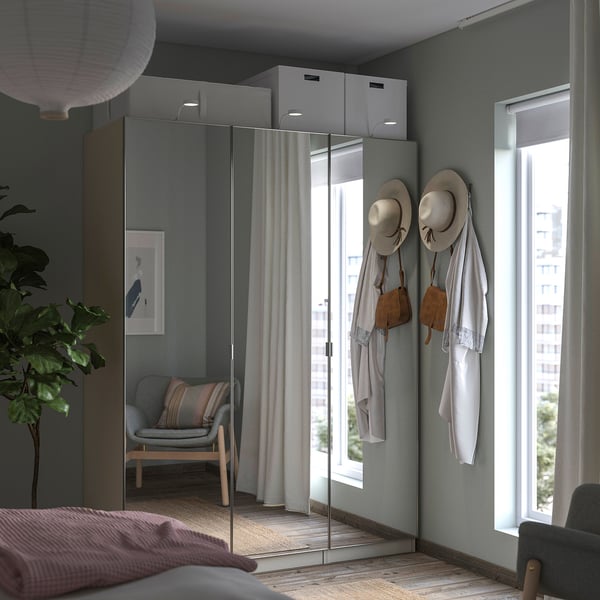 Dormitorio interior con armario gris PAX, portas de espello, sombreiros e bolsas colgantes, cadeira preto da xanela.