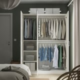 Armario branco ben organizado con roupa e obxectos dobrados en estantes e carrís colgantes. A parte superior ten tres colectores de almacenamento.