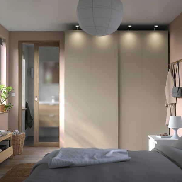 Dormitorio moderno con cama gris, gran armario incorporado con portas deslizantes e unha lámpada alta.