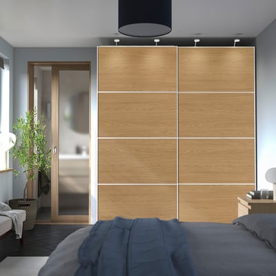 Dormitorio moderno con gran armario PAX de carballo. Decoración neutra, cama azul, porta de baño de vidro.