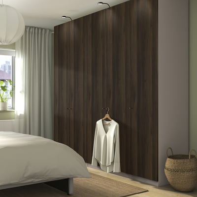 Dormitorio moderno con armario PAX alto e escuro, cama branca, lámpada colgante, cortina verde e cesta de vimbio.