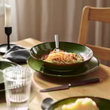 A cunca de cerámica verde contén a pasta co garfo; colocado sobre unha mesa de madeira con vidro, coitelo e cadeira.