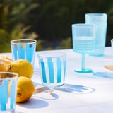 Vasos de cristal con raias azuis sobre unha mesa, perfectos para bebidas frías, con limóns e un pano branco preto.