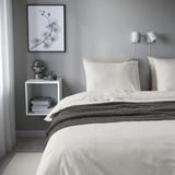 Cama minimalista con piñeiro branco, manta gris, luces nocturnas, arte, mesa de noite con libros, lámpada e frasco.