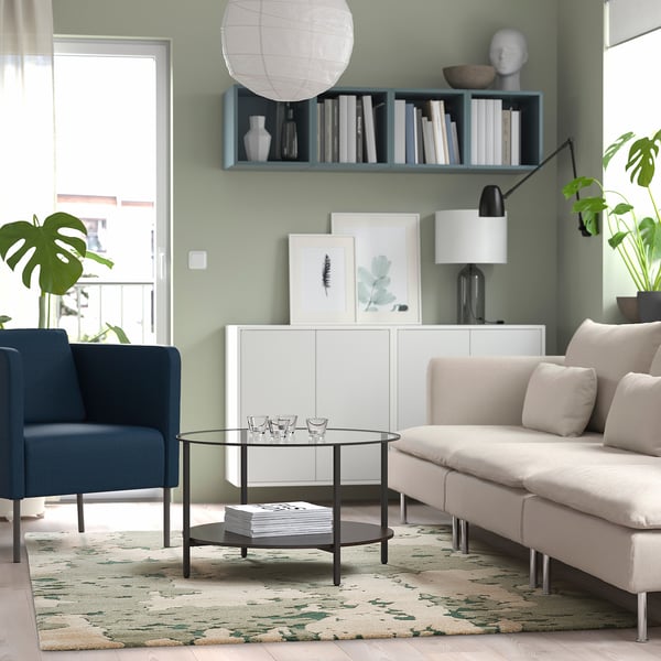 Sala de estar con alfombra abstracta verde, sofá beige, cadeira azul, mesa de café de vidro, sideboard branco.