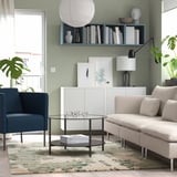 Sala de estar con alfombra abstracta verde, sofá beige, cadeira azul, mesa de café de vidro, sideboard branco.