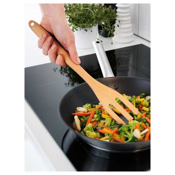 A persoa está a cociñar verduras de cores nunha tixola negra usando unha espátula de madeira.