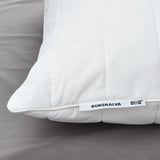 Primeiro plano da almofada IKEA RUMSMALVA sobre saba de cama gris.