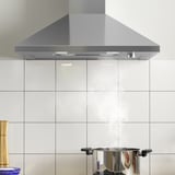 Capa de aceiro inoxidable con luz led montada sobre o backsplash da cociña de azulexos brancos.