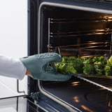 Persoa que coloca a bandexa de brócoli no forno usando luva de forno de silicona verde.