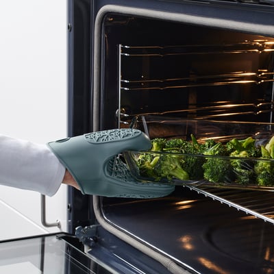 Persoa que coloca a bandexa de brócoli no forno usando luva de forno de silicona verde.