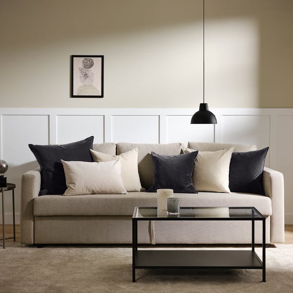 Sala de estar moderna con sofá beige, almofadas en branco e negro, mesa de café de vidro, luz colgante, obras de arte e alfombra beige.